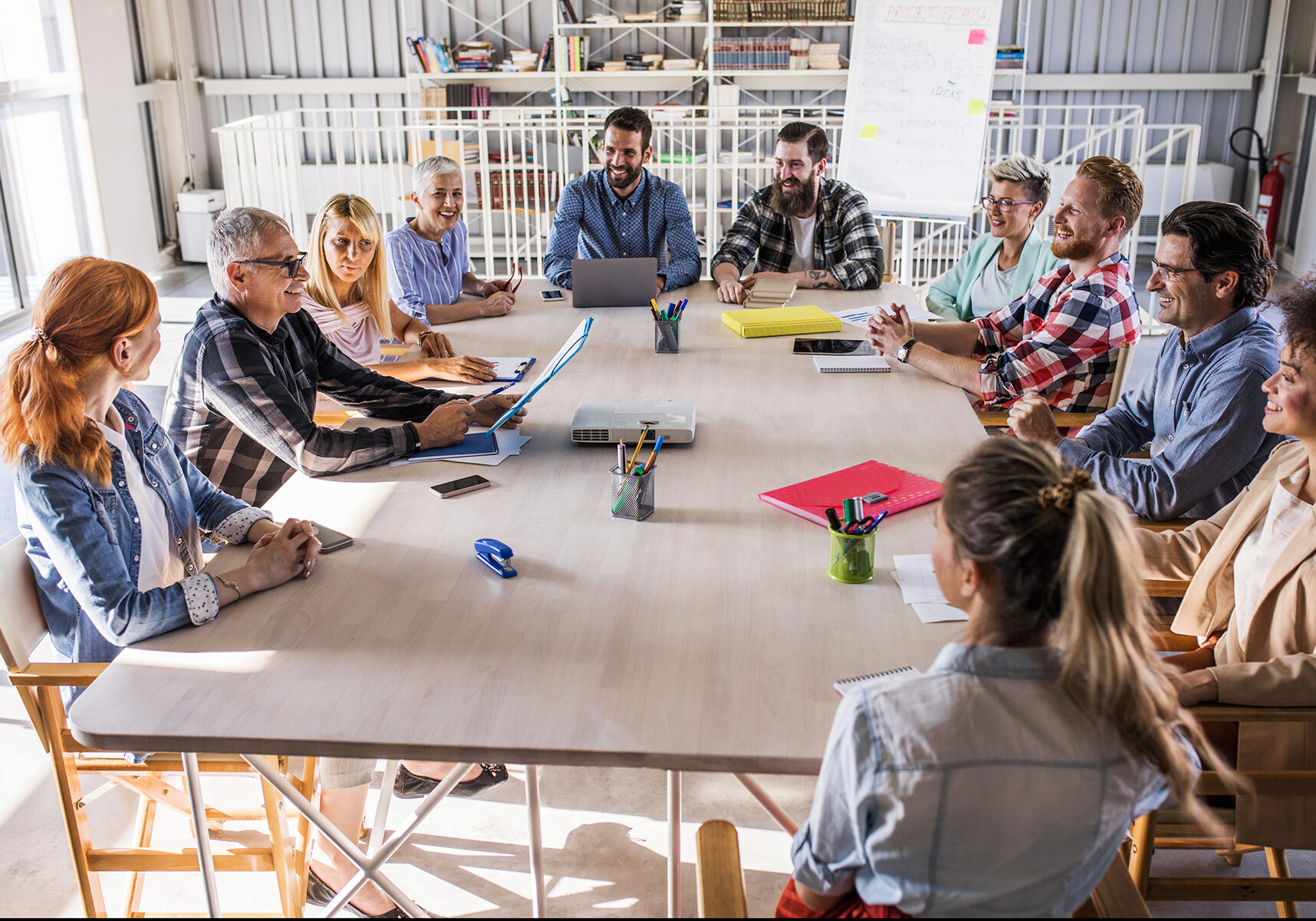 Large group of happy freelancers sitting at the table in the office and talking about new business plans.